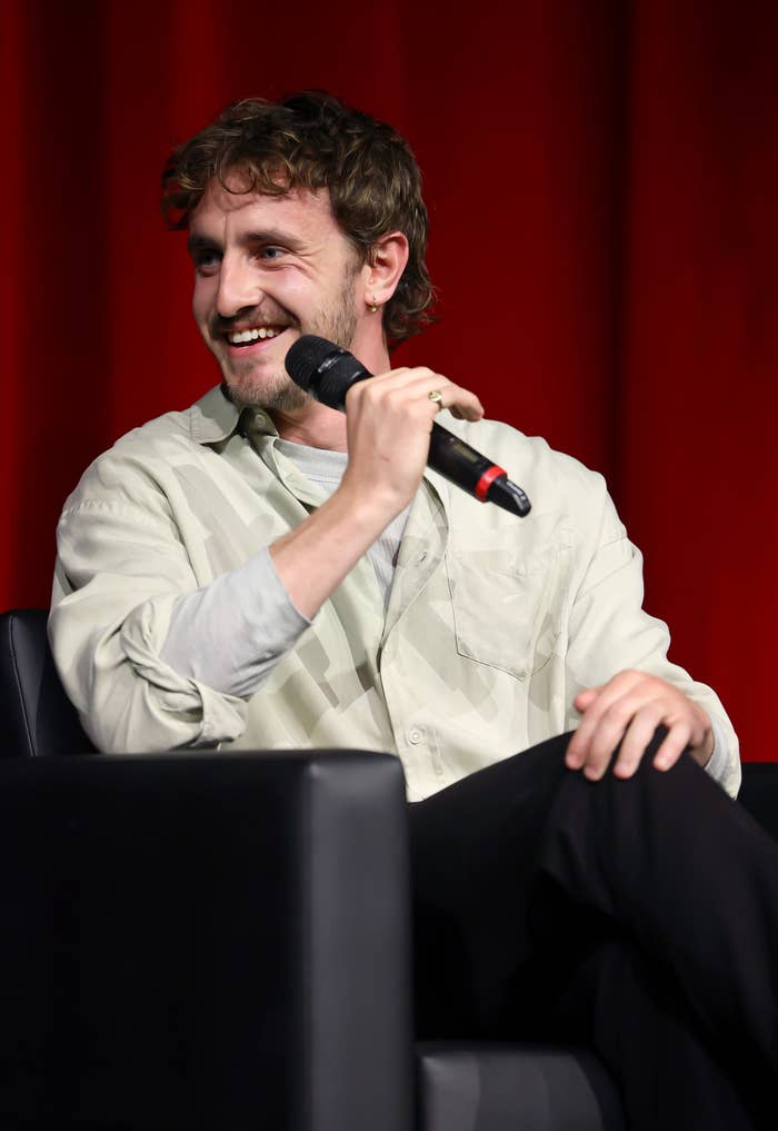 A closeup of Paul Mescal on a stage holding a microphone and smiling