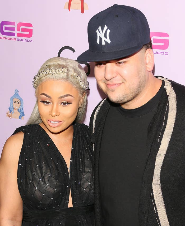 Rob Kardashian and Blac Chyna smiling on a red carpet, Blac Chyna in a braided hairstyle and black sheer dress, Rob Kardashian in a dark cap and jacket