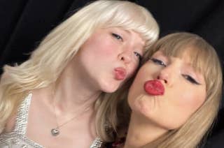 Taylor Swift and Maisie peters pose for a selfie, making kissy faces. Taylor wears a sequin dress; Maisie is in a white dress with silver detailing