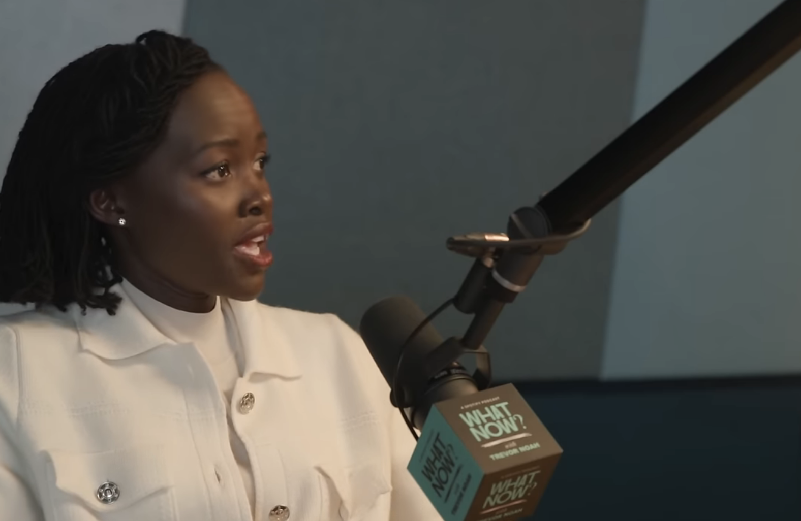 Lupita Nyong&#x27;o speaks into a microphone on the &quot;What Now? with Trevor Noah&quot; podcast