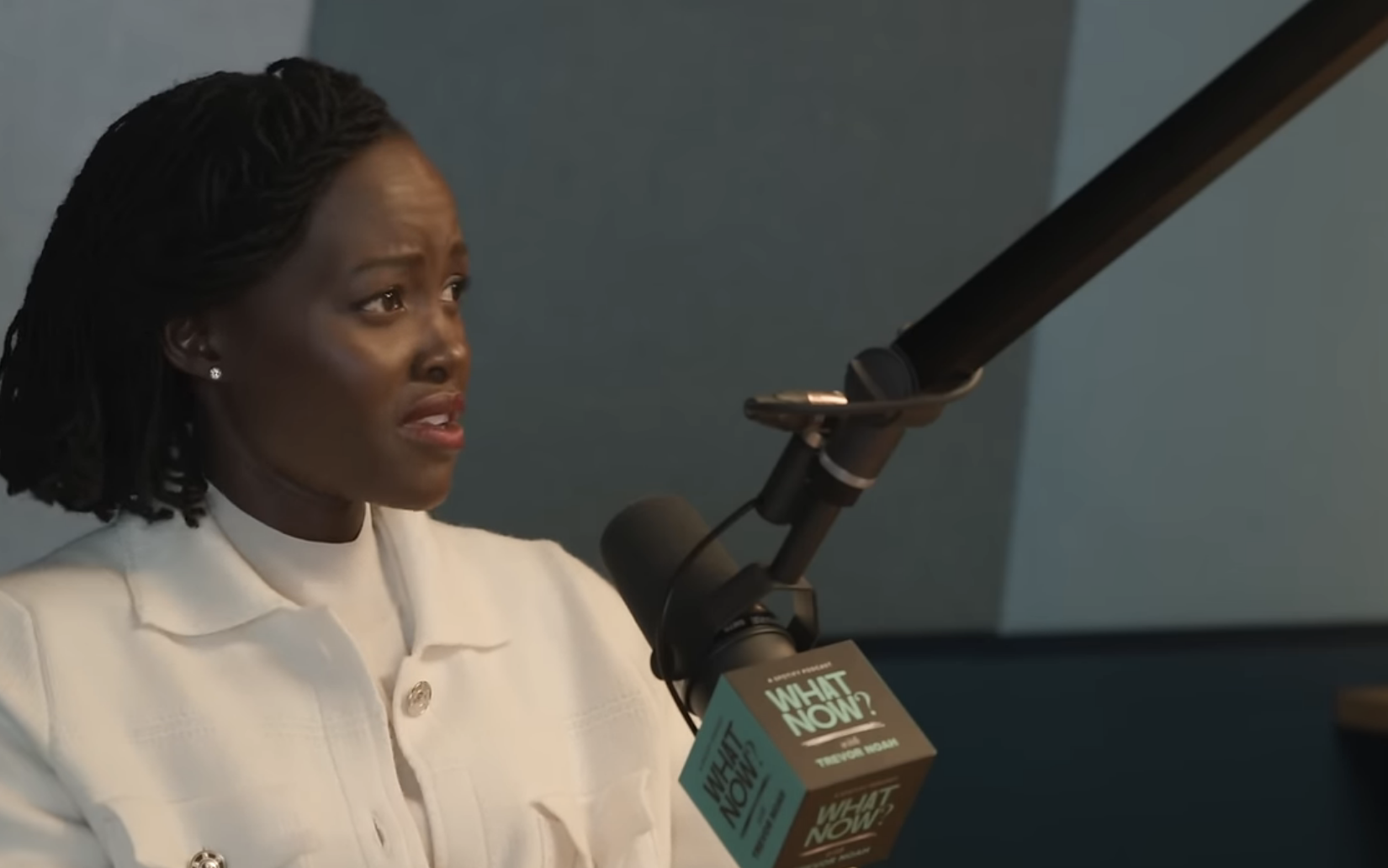 Lupita Nyong&#x27;o speaks into a microphone during the &quot;What Now?&quot; podcast with Trevor Noah, discussing African diaspora topics